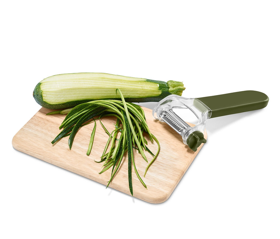 Eine halbe Zucchini liegt auf einem Brett neben geschnittenen Streifen und einem 3-in-1-Universalschäler.
