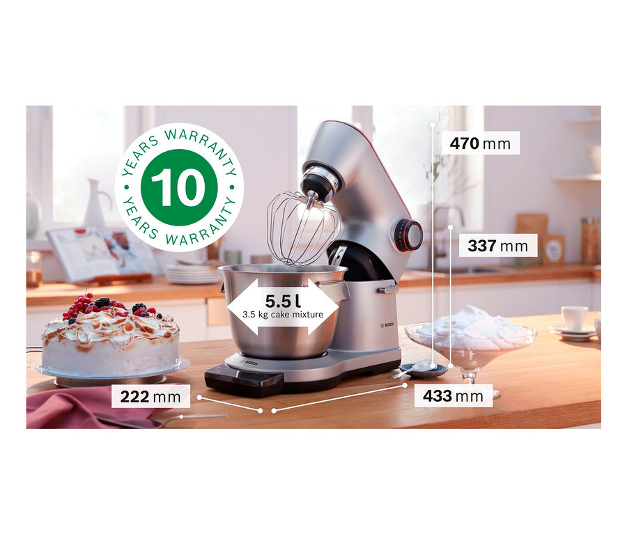 Eine silberne Bosch Küchenmaschine MUM9DT5S41 mit Schüssel und Schneebesen steht auf einer Küchentheke neben einem Kuchen und einer Schüssel mit Sahne.