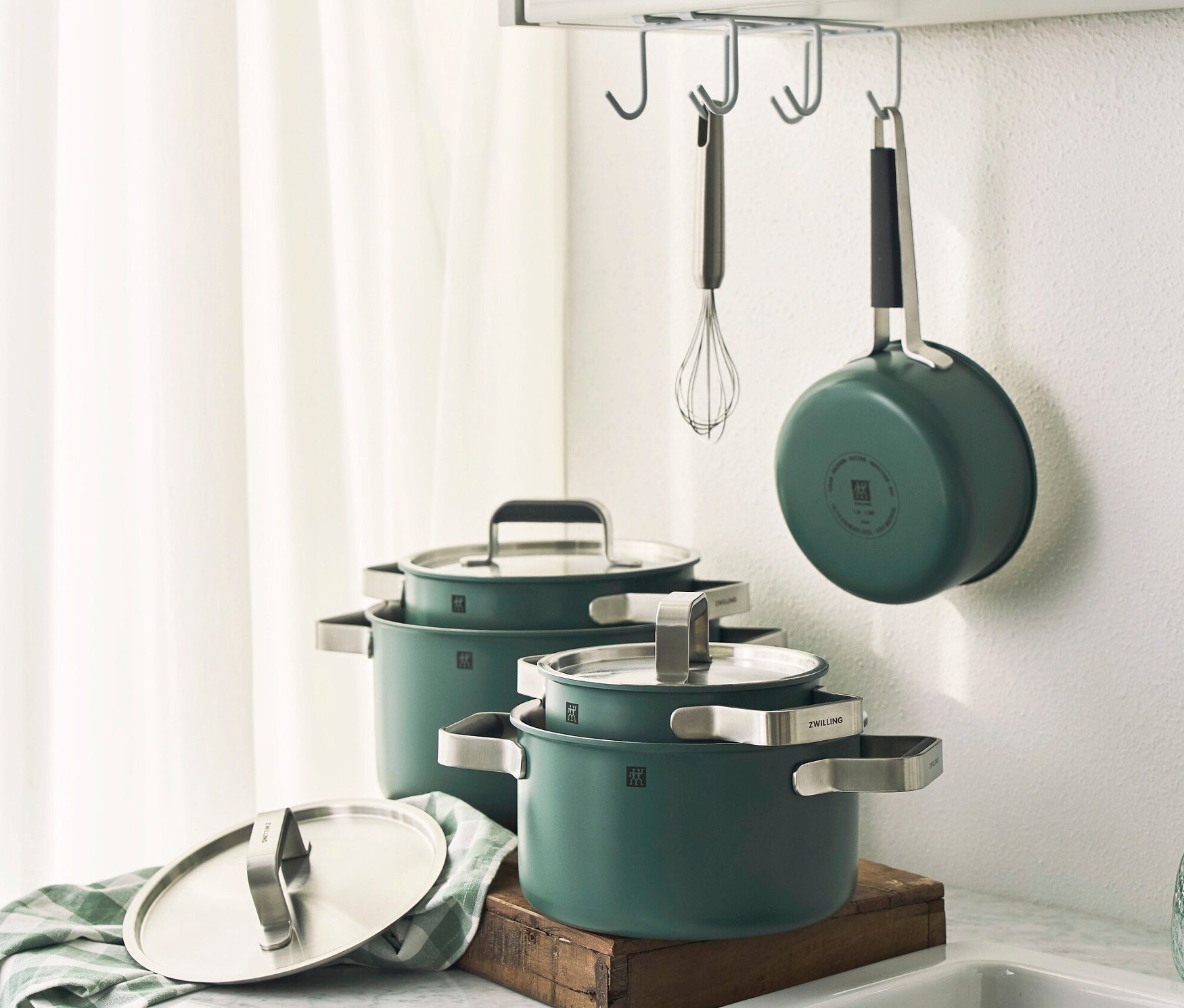 Grünes, fünfteiliges ZWILLING PURE Edelstahl-Kochgeschirr-Set auf Marmorplatte neben weißem Spülbecken.