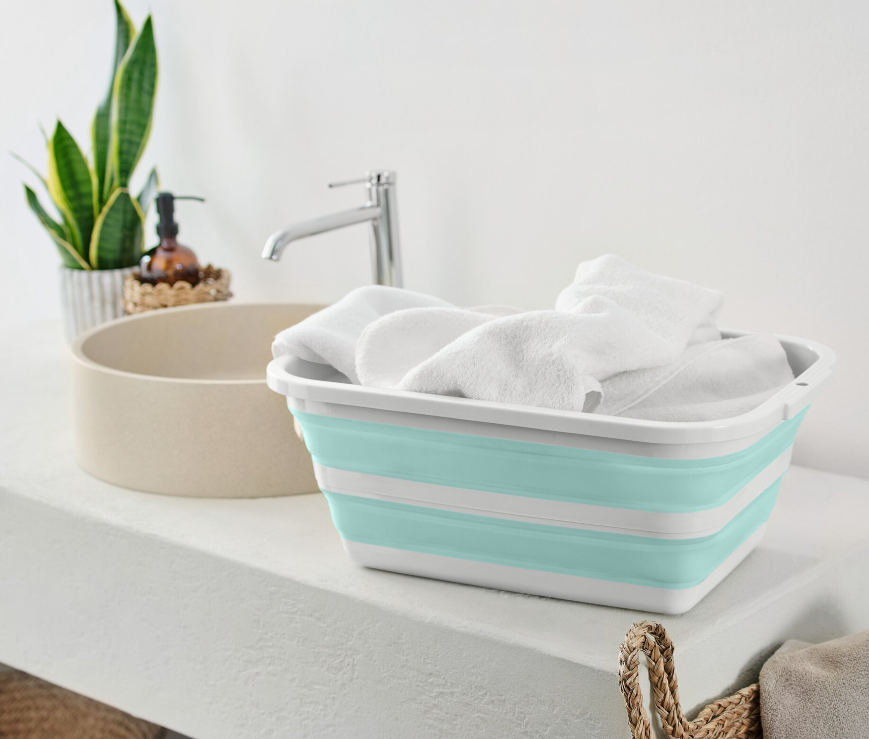 Ein faltbarer Wäschekorb, gefüllt mit weißen Handtüchern, steht auf einem weißen Regal neben einem Waschbecken.