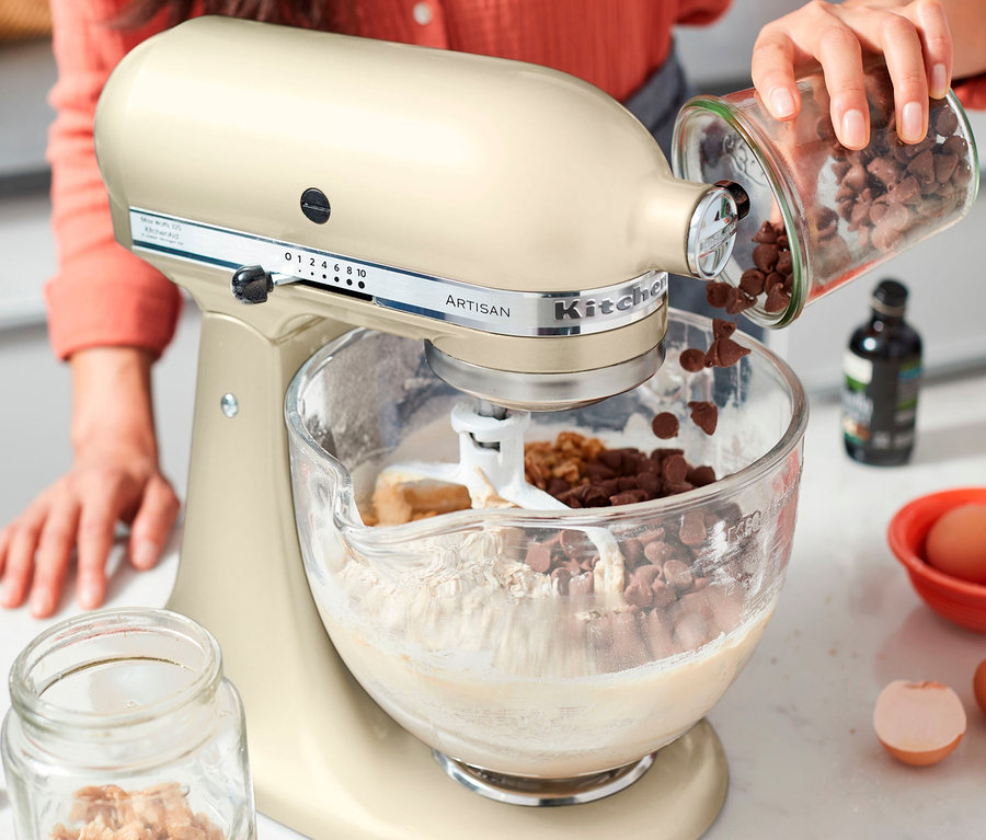 Frau gießt Schokoladenstückchen in die Schüssel einer creme farbenen KitchenAid Artisan Küchenmaschine.