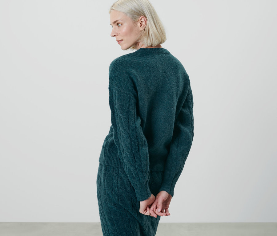 Frau posiert von hinten mit petrolfarbenem Strickpullover.