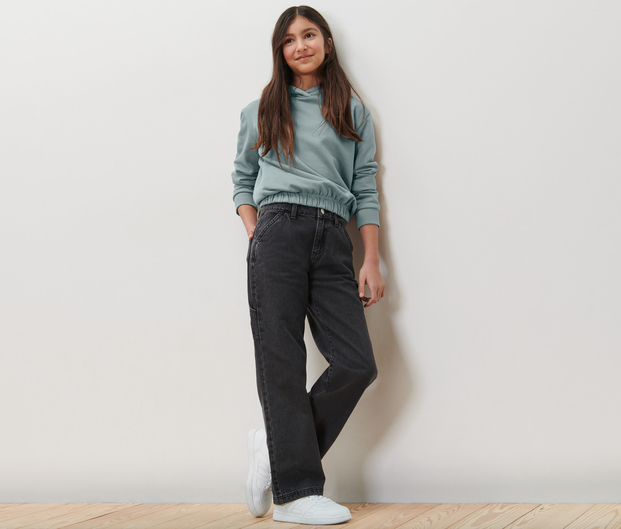 Mädchen posiert in Kinder-Cargohose und Hoodie.