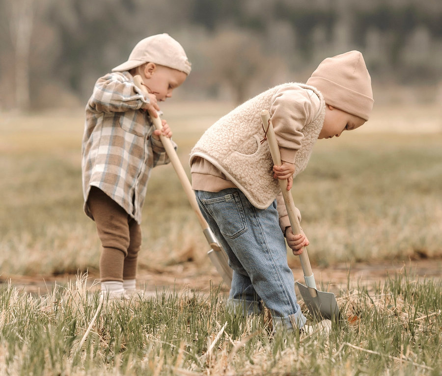 Zwei kleine Kinder spielen draußen auf einer Wiese mit einem großen Gartenwerkzeug-Set von Small Foot.