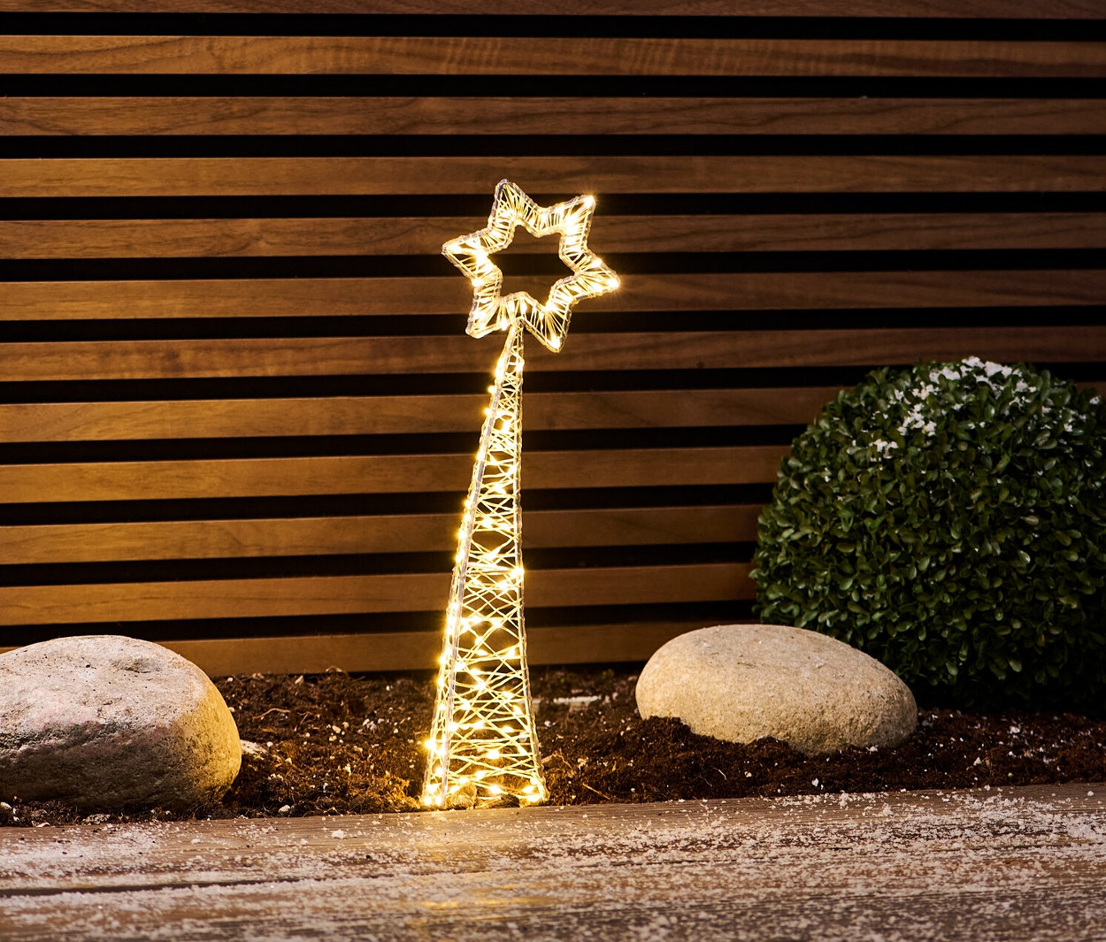 Eine kleine LED-Sternschnuppe steht zwischen Steinen und einem Busch.