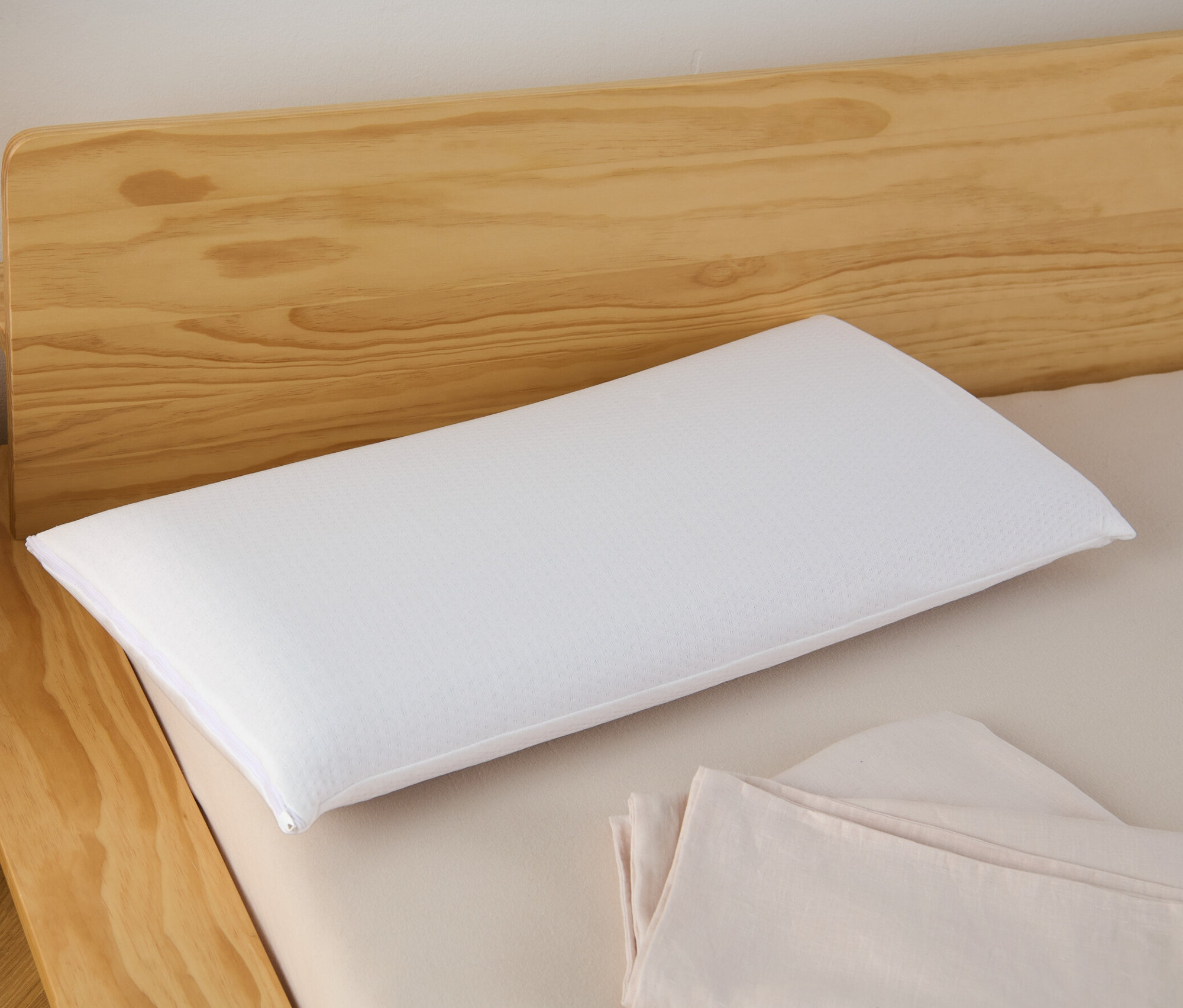Ein weißes Visko-Komfortkissen liegt auf einem Bett mit hölzernem Kopfteil.