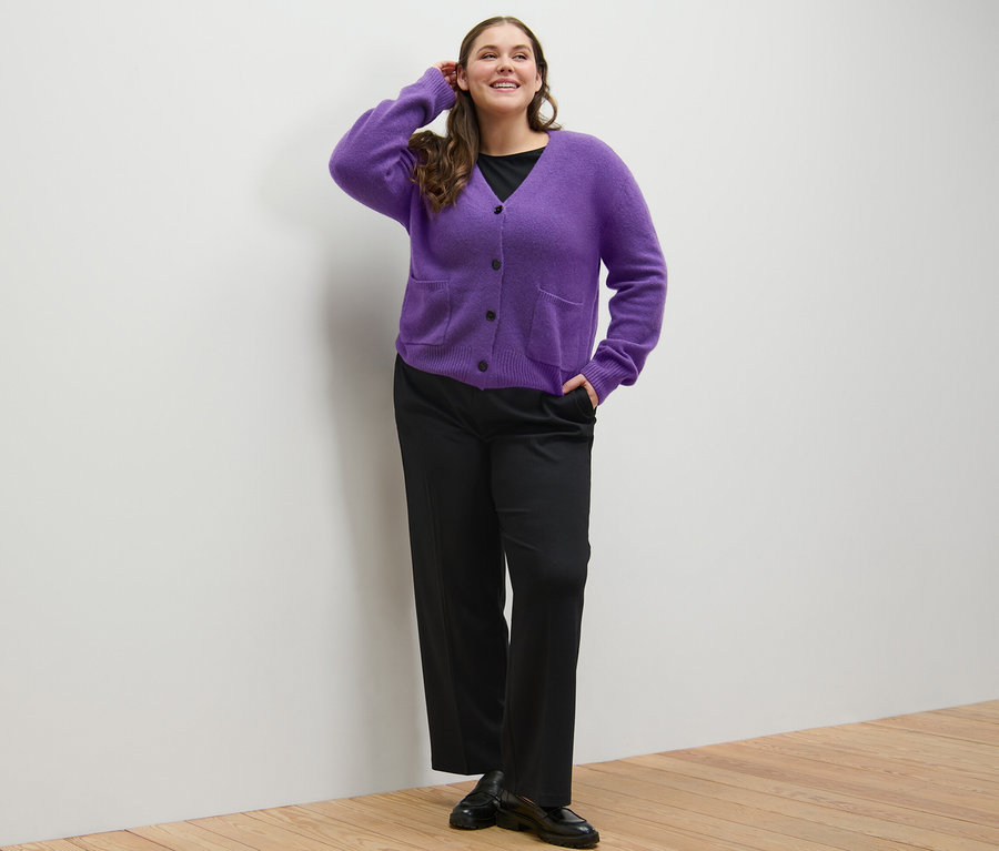 Frau posiert in schwarzem Shirt mit 3/4-Arm, Komfort-Jerseyhose und lila Strickjacke mit Wolle.