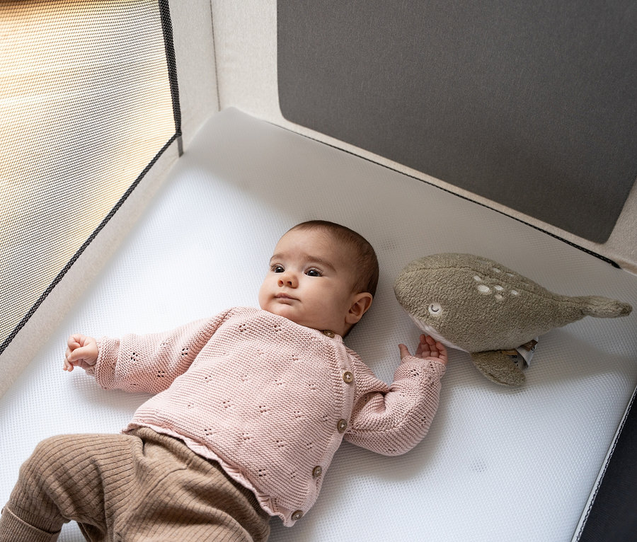 Ein Baby liegt im Osann Kid's Alm Kinderreisebett »Fresh Air« inkl. Matratze und spielt mit einem Wal-Spielzeug.