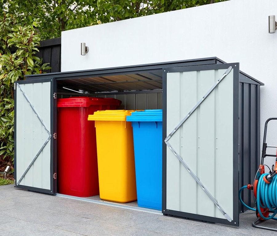 Geöffnete Gerätebox mit rotem, gelbem und blauem Behälter, daneben Rasenmäher und Schlauchaufroller.