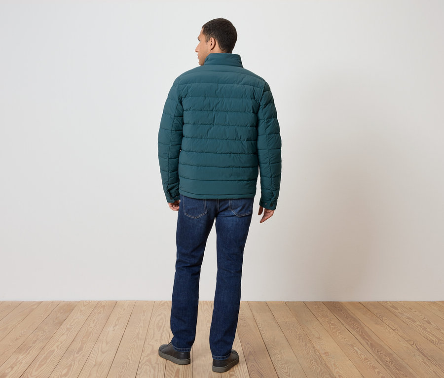 Mann von hinten trägt eine grüne Daunenjacke, Jeans und Schuhe.