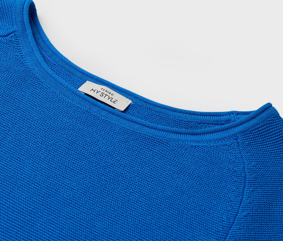 Detailaufnahme eines blauen Pullovers mit Rundhalsausschnitt und einem Etikett mit der Aufschrift MY STYLE.