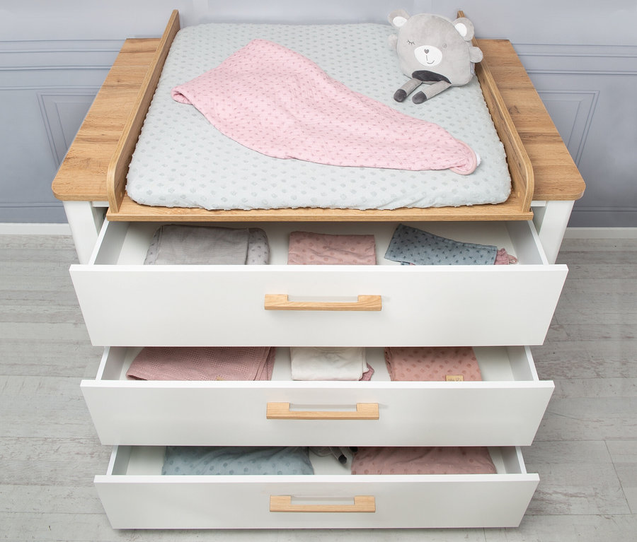 Ein Wickeltisch mit offenen Schubladen, einer Auflage und einem Plüschbären. In den Schubladen befindet sich Babykleidung. Teil eines roba Kinderzimmer-Sets »Ava« mit Bett, Wickelkommode, Schrank.