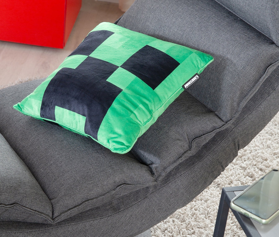 Ein grünes Minecraft Creeper Dekokissen liegt auf einem grauen Stoffstuhl.