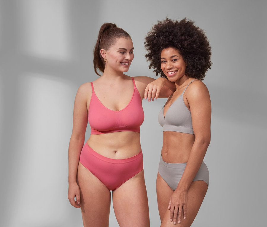 Zwei Frauen posieren nebeneinander. Eine trägt einen Seamless-Schalen-BH und Seamless-Pantys in Pink. Die andere trägt einen Seamless-Bustier und Seamless-Pantys in Grau.
