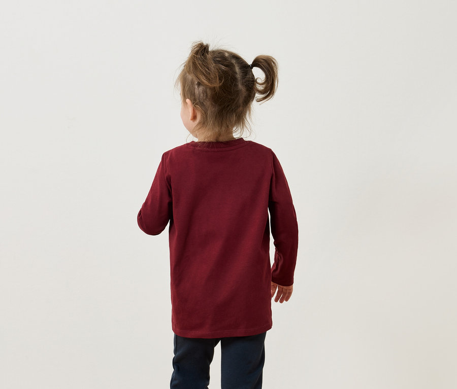 Rückansicht eines kleinen Mädchens mit Zöpfen, das ein weinrotes Langarmshirt und dunkelblaue Hosen trägt.
