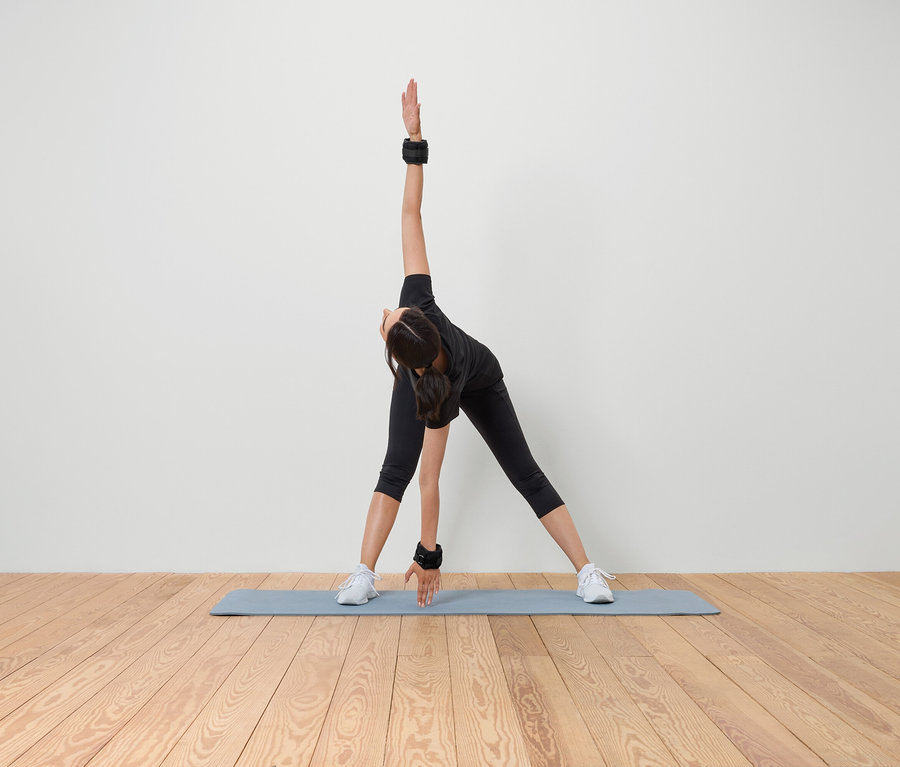 Frau dehnt sich auf einer Matte mit Gewichten an Handgelenk und Knöchel.