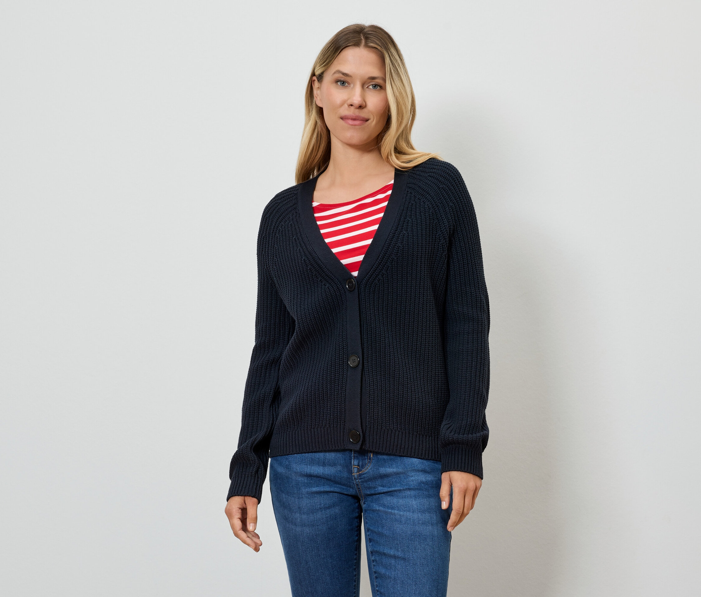 Eine Frau trägt eine dunkelblaue Strickjacke über einem rot-weiß gestreiften T-Shirt und Jeans.
