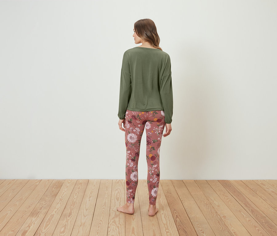 Eine Frau steht mit dem Rücken zur Kamera und trägt ein olivgrünes Langarmshirt und Leggings mit Blumenmuster.