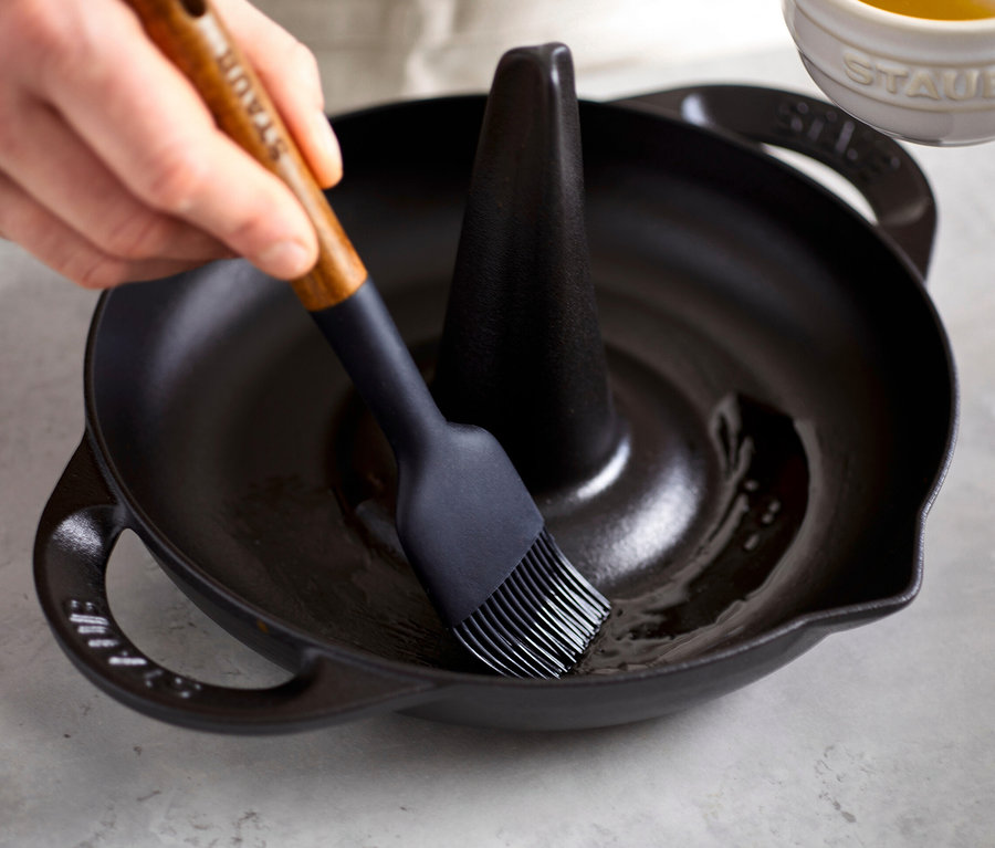 Eine Hand pinselt Öl in einem schwarzen STAUB Hähnchen-Bräter.