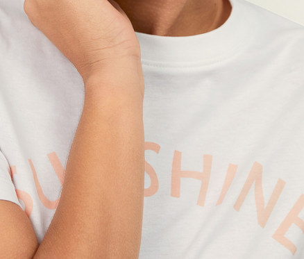 Lächelnde Frau berührt ihr Gesicht und trägt ein T-Shirt mit Print.