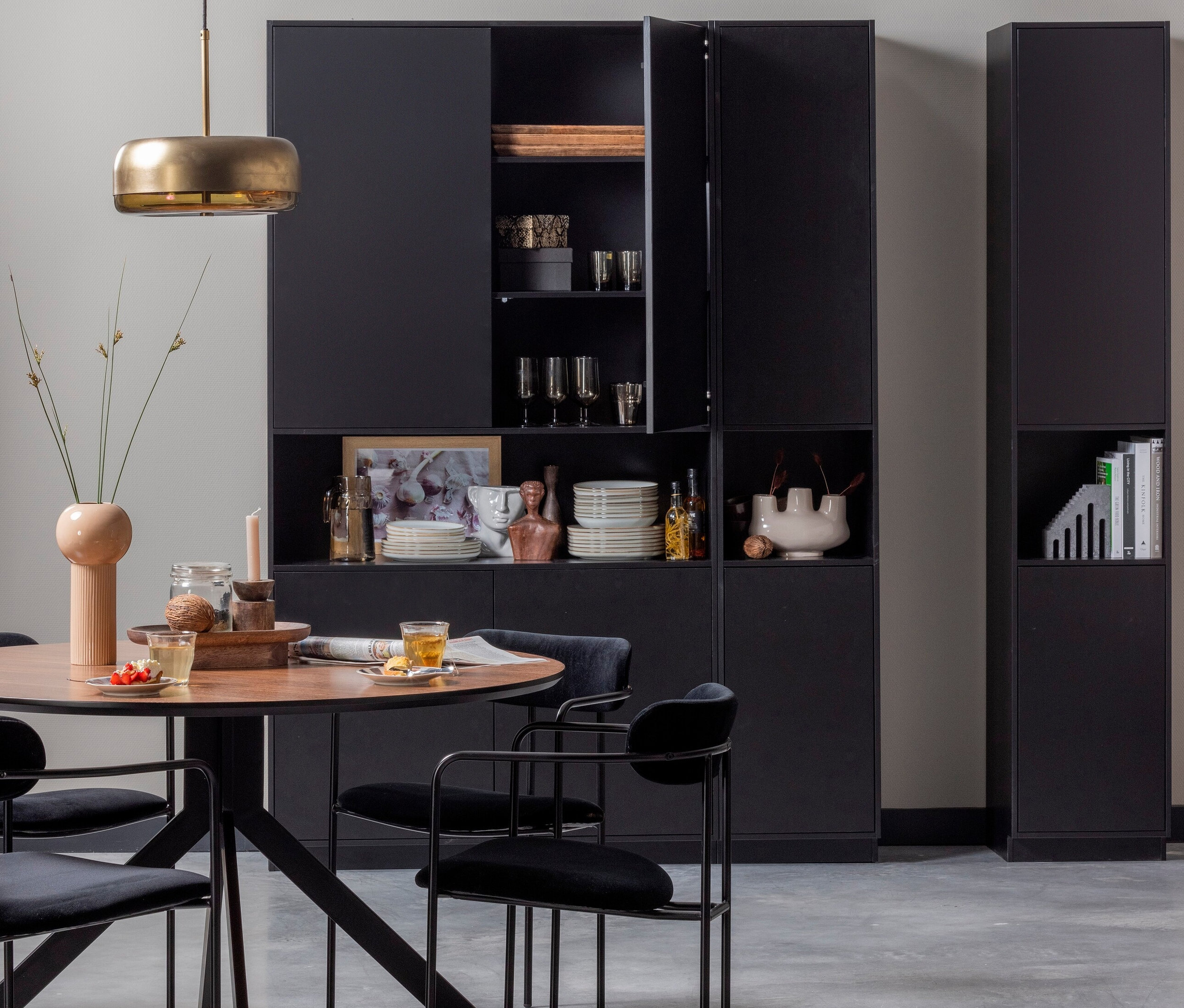 Schwarzer Esstisch mit vier schwarzen Woood Ivy Samtstühlen vor einem schwarzen Schrank.