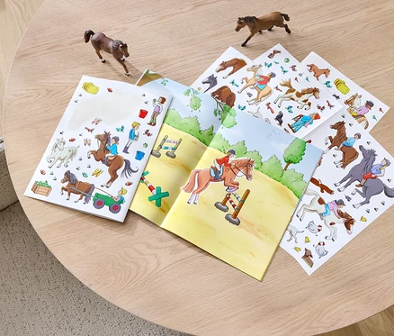 Ein geöffnetes Stickerbuch »Pferde und Ponys« liegt auf einem Tisch, daneben zwei Pferdefiguren.