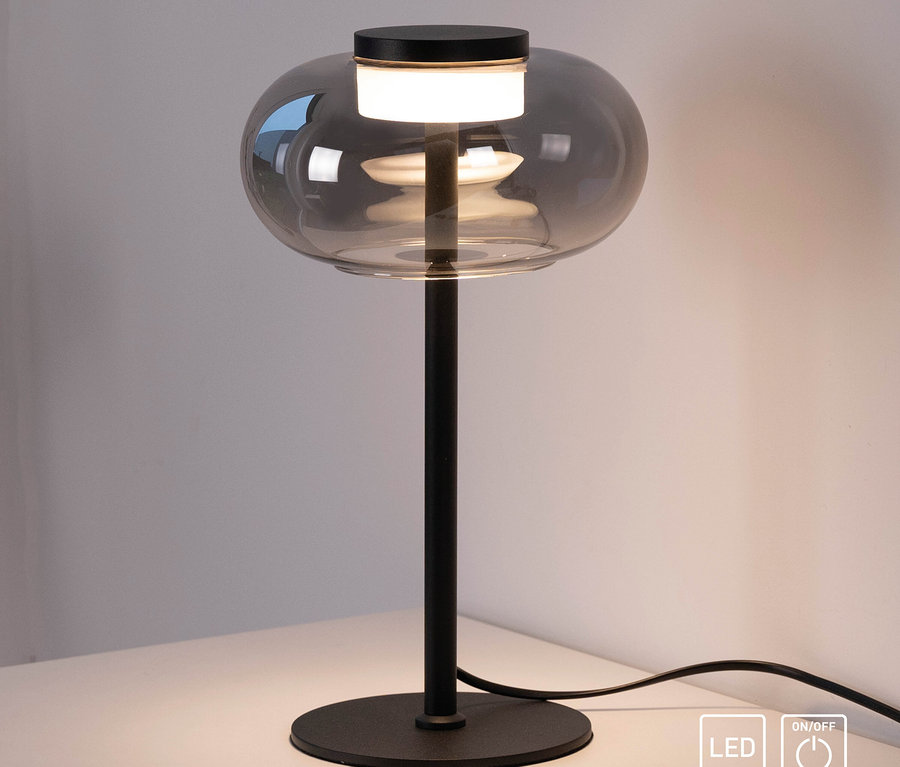 Eine schwarze Tischleuchte mit einem kugelförmigen Glasschirm steht auf einem weißen Tisch.