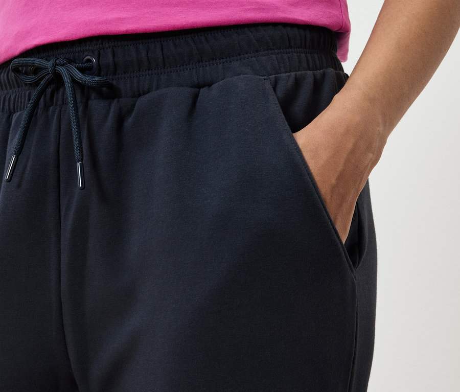 Detailaufnahme einer dunkelblauen Trainingshose mit Hand in der Tasche und rosafarbenem T-Shirt.