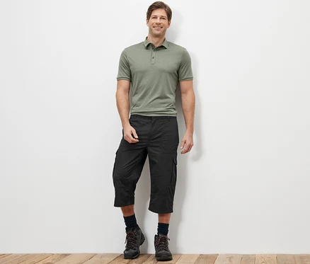 Ein Mann steht und trägt ein grünes Poloshirt und eine anthrazitfarbene Cargo-Bermuda in 3/4-Länge.