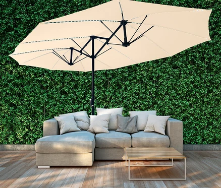 Beiger LECO Doppel-Sonnenschirm* mit LED-Beleuchtung, oval, ca. 270 x 460 cm, über grauem Sofa mit Kissen.