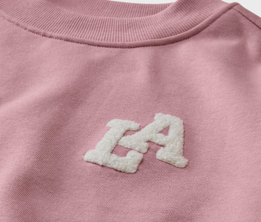 Detailansicht eines Kinder-Sweatshirts mit angerauter Innenseite in Rosa mit weißem "LA"-Schriftzug.