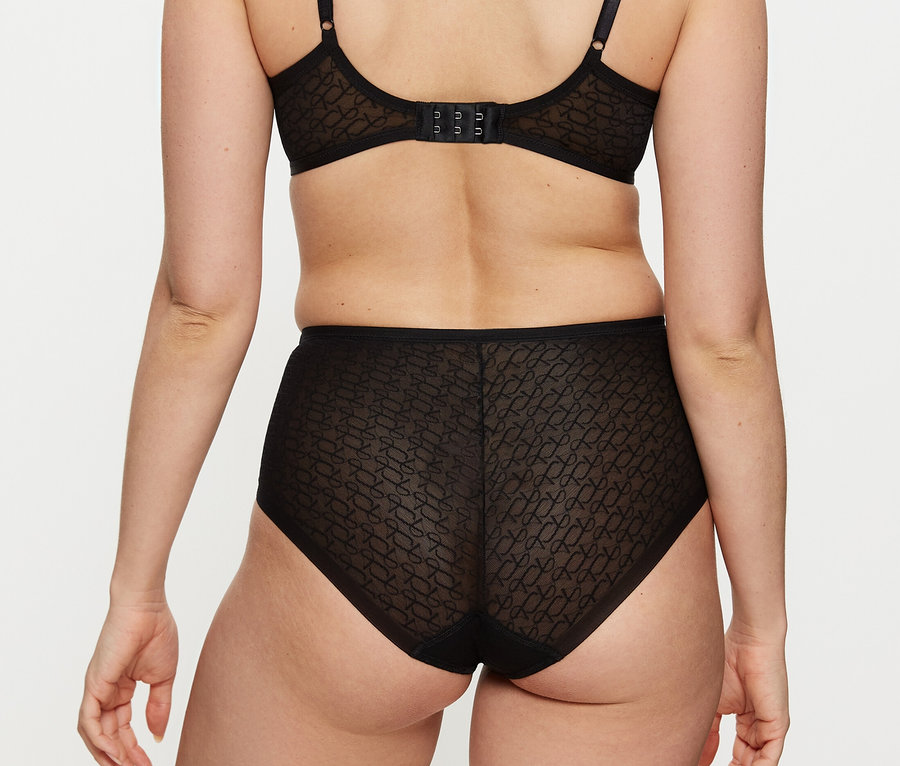 Frau von hinten in schwarzem, gemustertem BH und schwarzem, transparentem Triumph Signature Sheer Maxi EX Slip mit Muster.