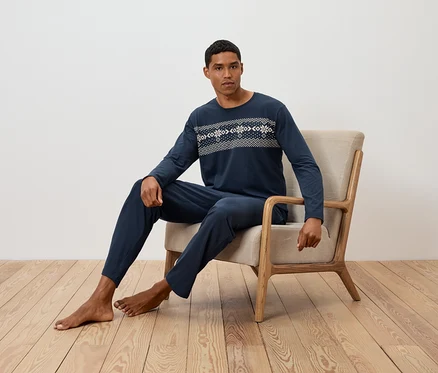 Mann sitzt in einem Sessel und trägt einen dunkelblauen, langärmeligen Pyjama mit Muster.