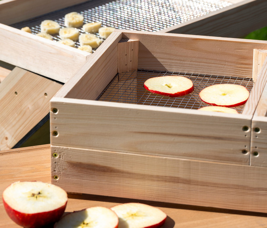 Zwei Solar-Dörrschränke aus Holz mit Apfel- und Bananenscheiben.