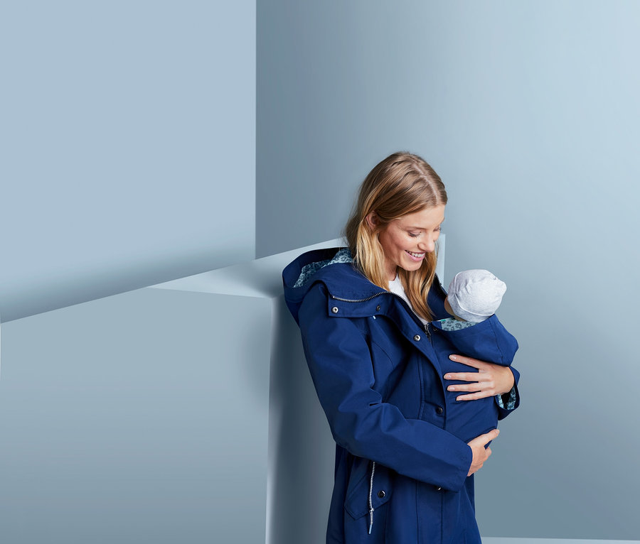 Frau hält Baby in Umstands-Regenjacke.