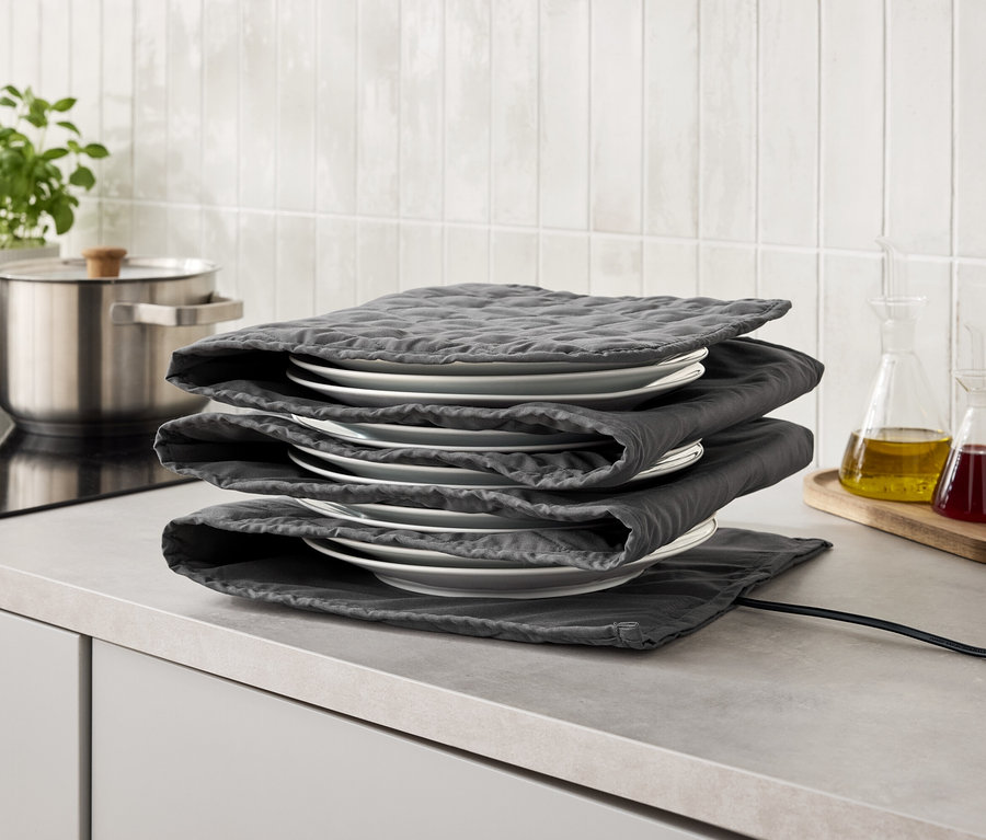 Ein Stapel weißer Teller, umwickelt mit grauen Stoffunterlagen, steht auf einer grauen Küchentheke.
