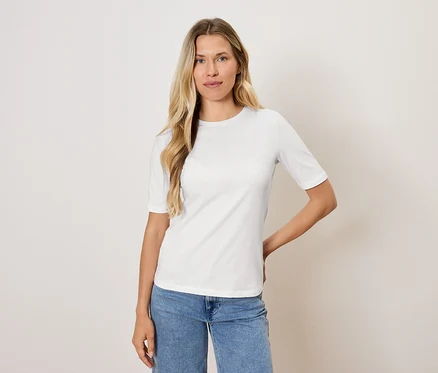Frau mit blonden Haaren posiert in einem weißen T-Shirt und blauen Jeans.