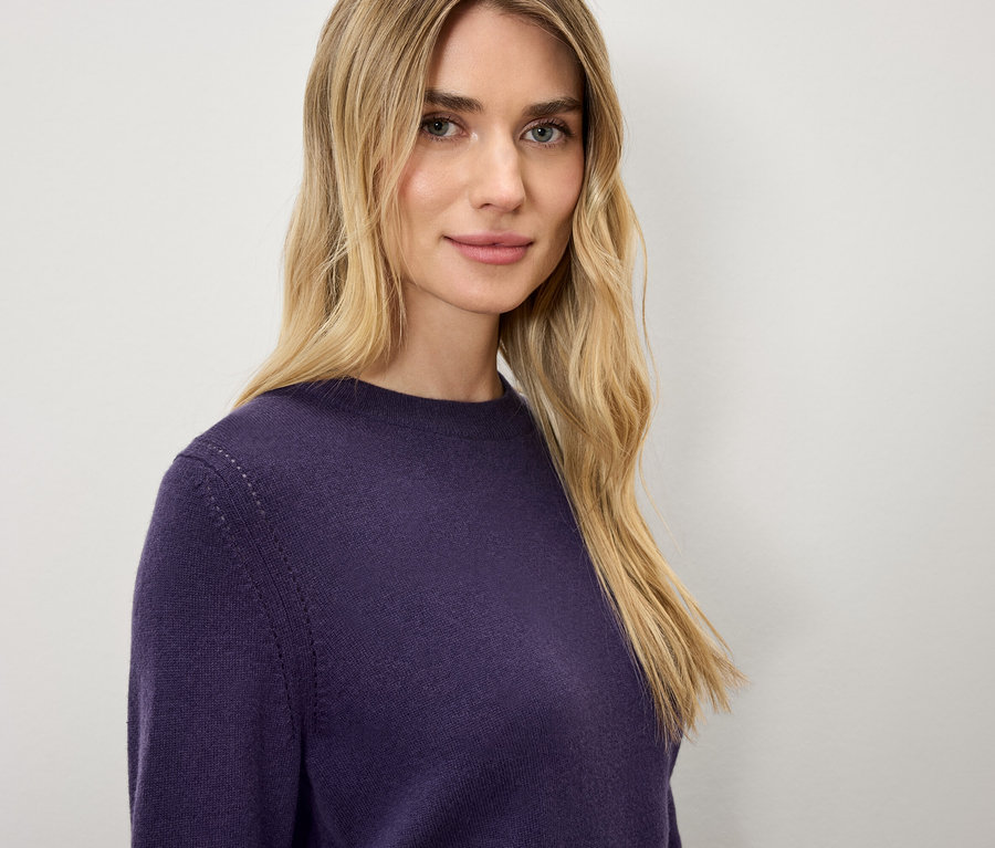 Blonde Frau in einem dunkelvioletten Pullover.
