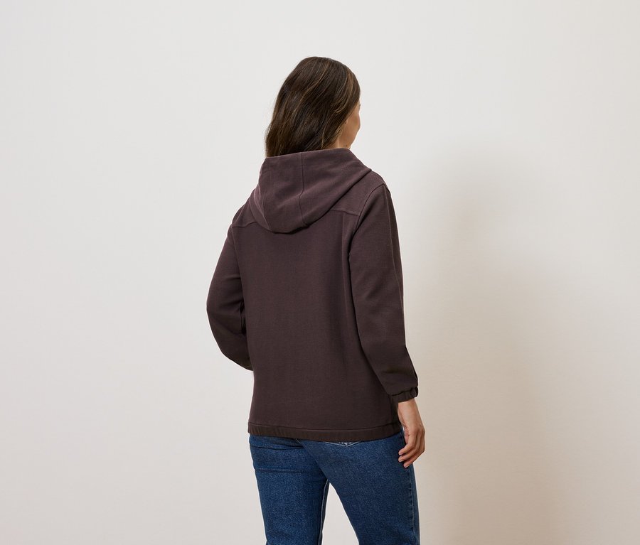 Eine Frau steht mit dem Rücken zur Kamera und trägt einen braunen Hoodie und Jeans.