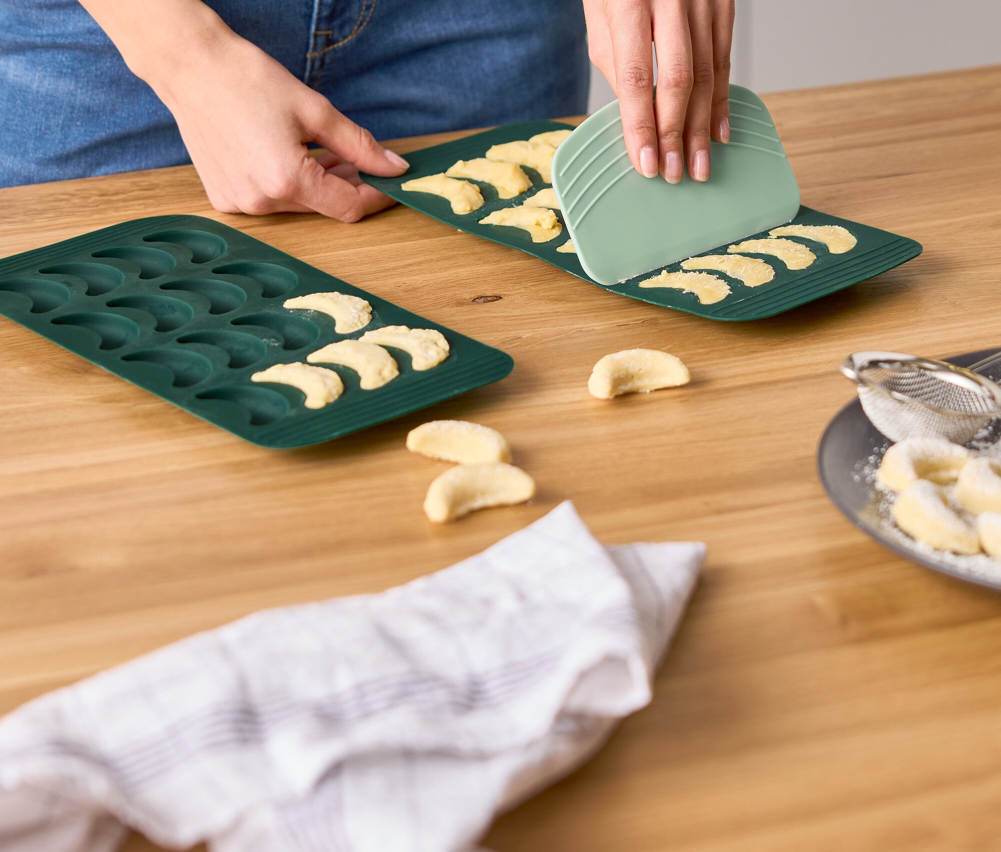 Frau verwendet einen grünen Schaber, um Kekse aus einer halbmondförmigen Keksform zu lösen.