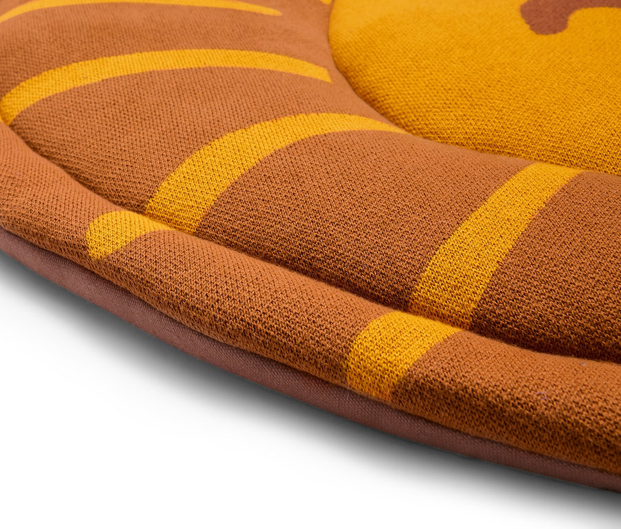 Detailansicht eines runden, braunen Kissens mit gelben Streifen.