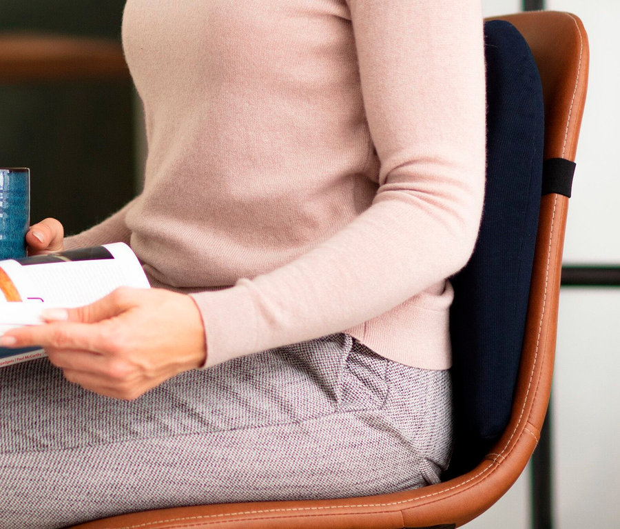 Frau sitzt mit TEMPUR® Lordosekissen auf einem braunen Stuhl und liest.