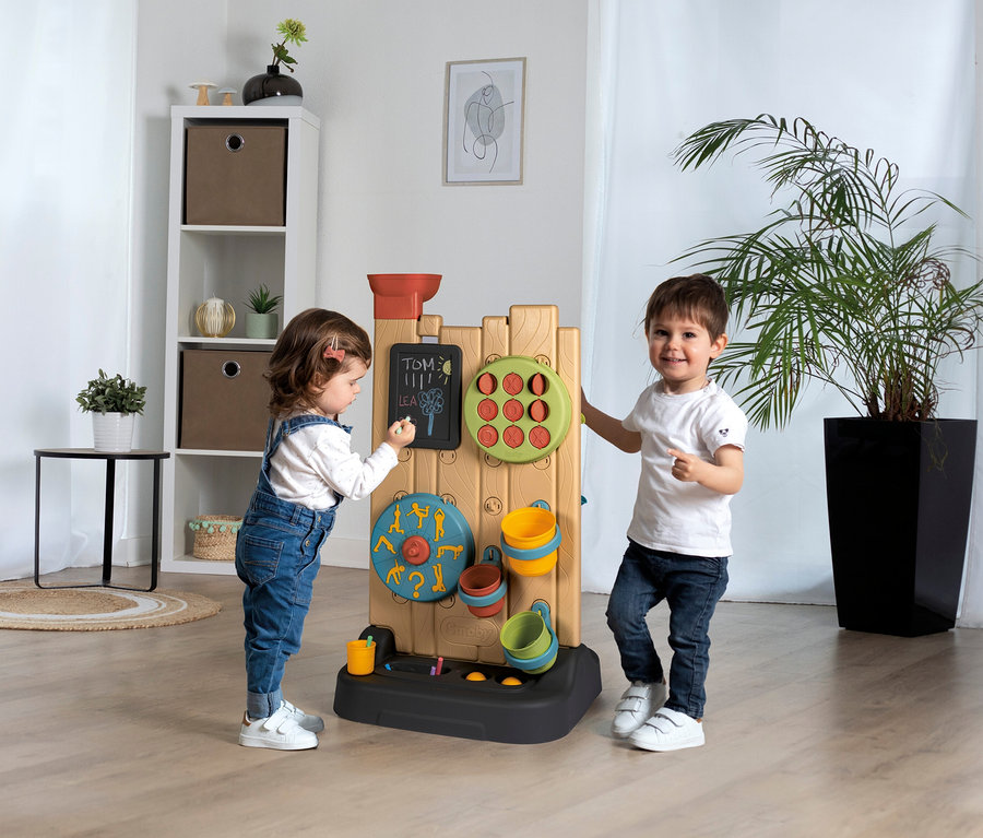 Junge und Mädchen spielen mit der Smoby Life Activity Wall. Das Mädchen malt auf die Tafel, der Junge steht daneben.