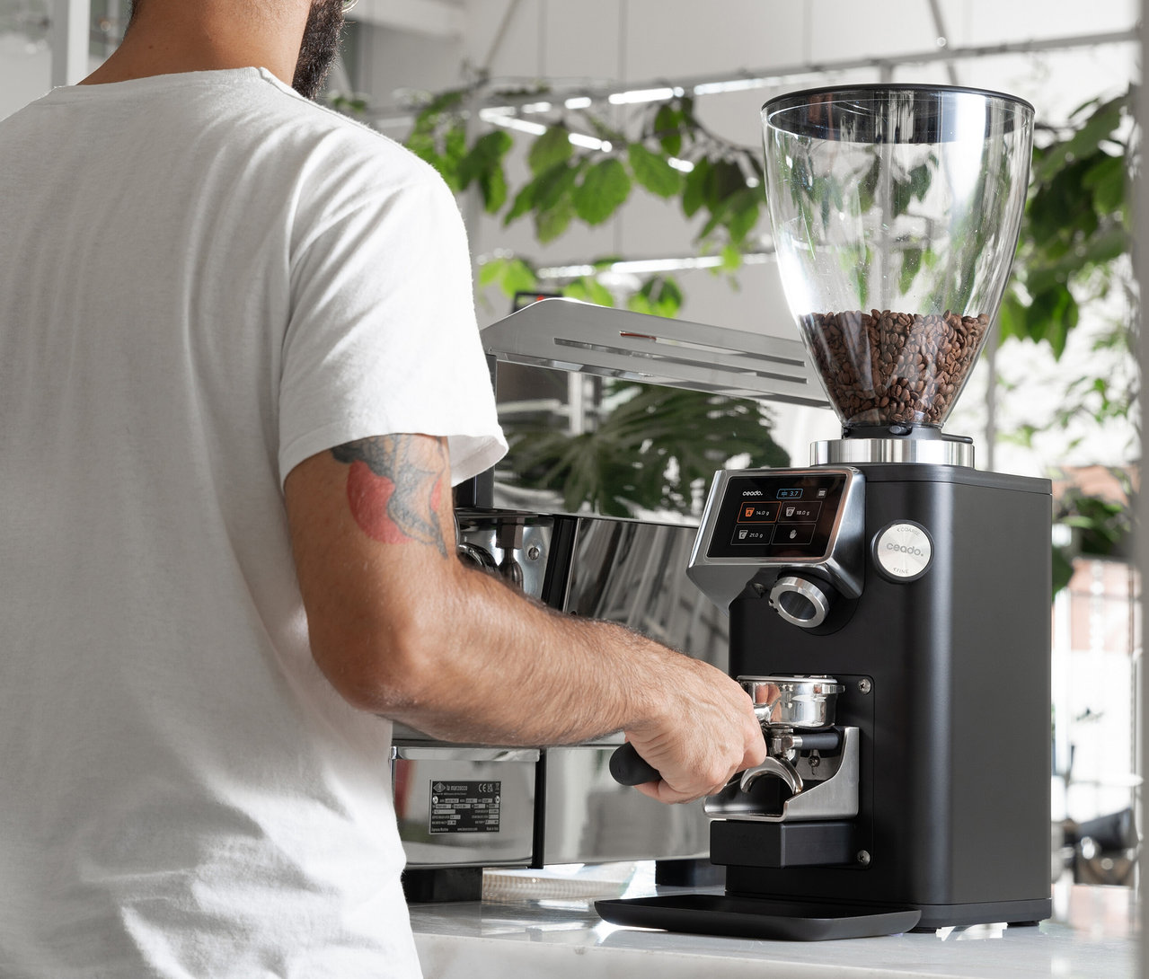 Mann bedient eine schwarze Ceado Kaffeemühle mit Kaffeebohnen im Trichter.