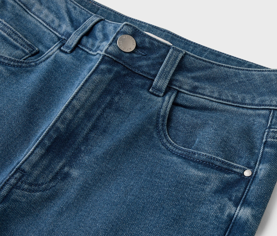 Nahaufnahme von blauen Jeans mit Knopf und Tasche vor einem weißen Hintergrund.