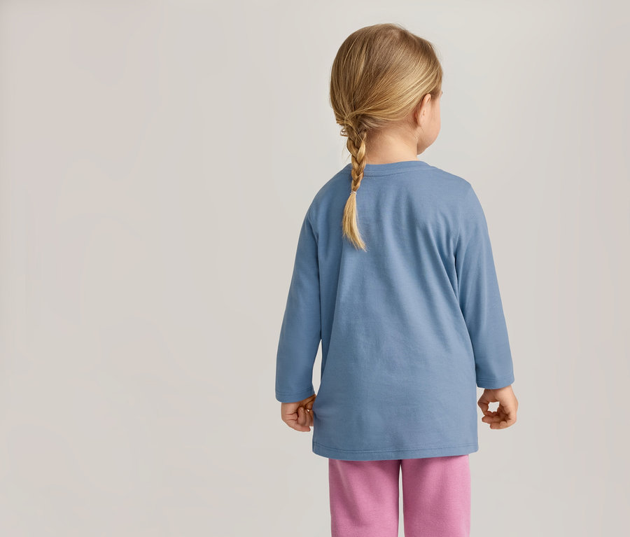 Rückansicht eines Kindes mit Zopf, das ein blaues Langarmshirt und eine pinke Hose trägt.