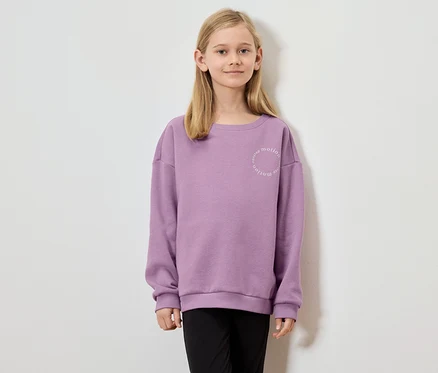 Mädchen mit blonden Haaren trägt ein lila Sweatshirt mit der Aufschrift "nonstop motion".