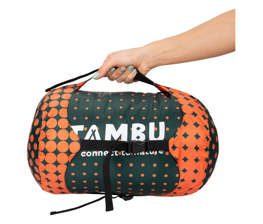 Eine Hand hält einen grünen Schlafsack mit orangen Punkten.