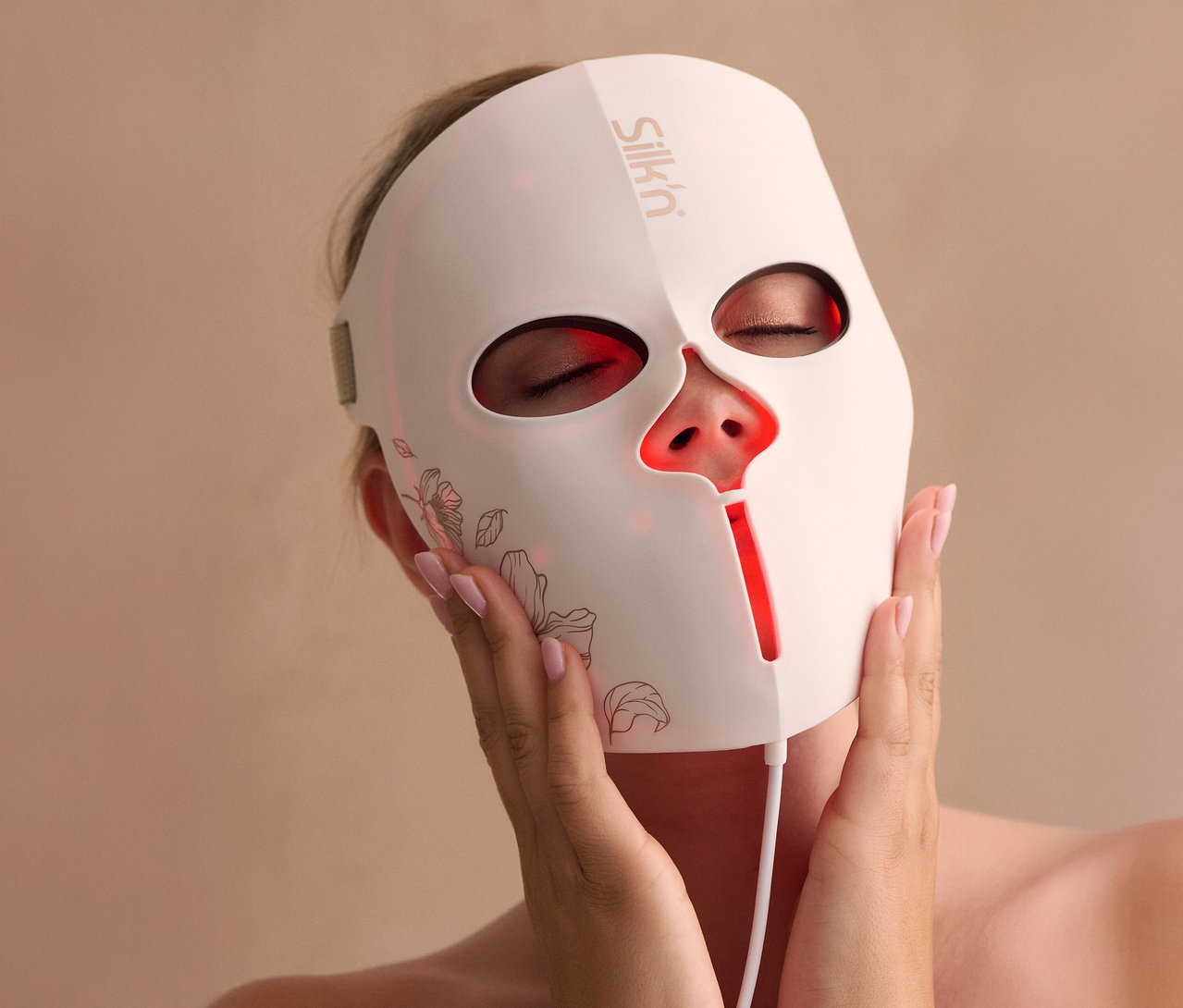 Frau hält Silk'n LED Gesichtsmaske mit EMS vor ihr Gesicht.