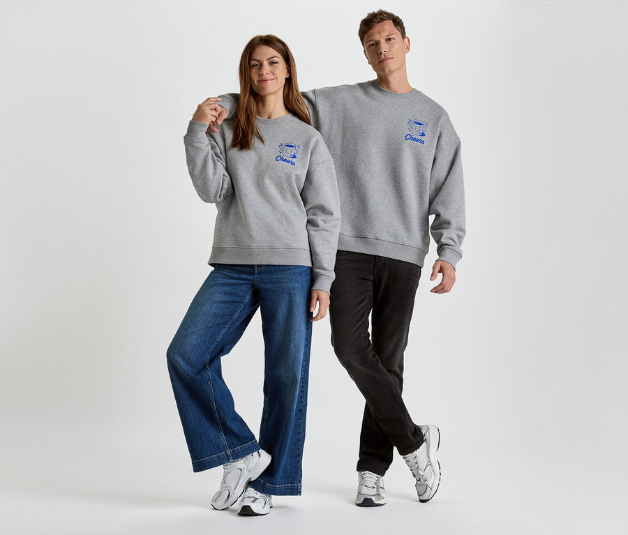 Frau und Mann stehen nebeneinander und tragen graue Sweatshirts mit blauen "Cheers"-Aufdrucken, kombiniert mit Jeans und Turnschuhen.